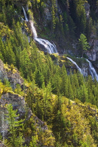Waterfall cascading down a lush green mountain slope in a forest in Altai mountains in summer in the Altai Republic, Siberia, Russia