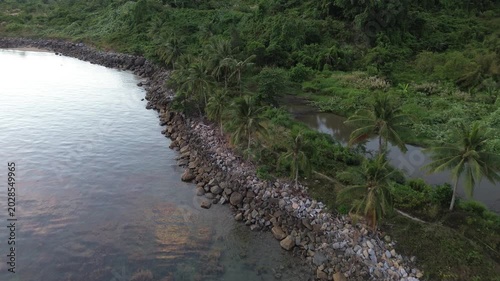Tropical landscape featuring rocky beach and palm trees at dusk