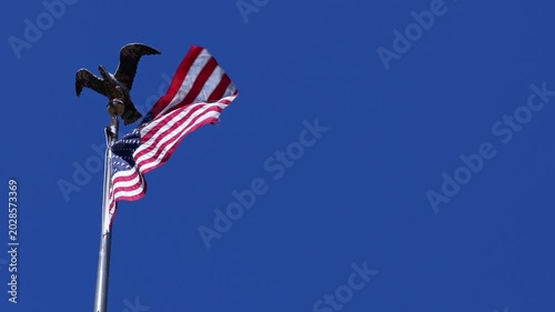 American flag waving in breeze with eagle statue against blue background in Fairmont, West Virginia