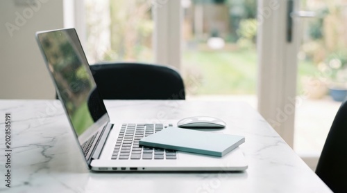 Modern laptop with closed notebook on top resting on white marble surface in bright home office environment for productive remote work and study habits setting