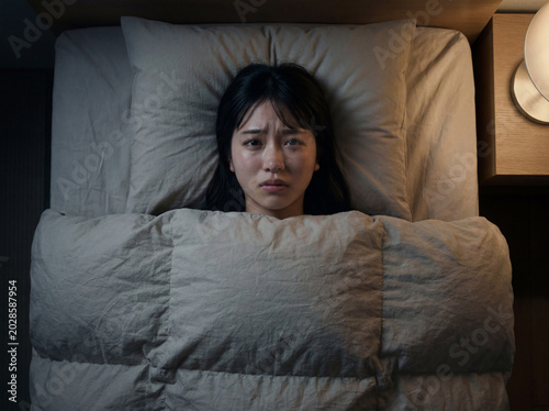 ベッドで眠れず不安な表情を浮かべる若い女性、不眠症や悩みのイメージ