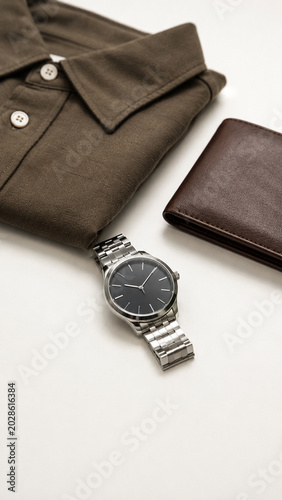 Earthy Elegance: A meticulously folded dark olive shirt rests alongside a sleek silver wristwatch and a classic brown leather wallet, exuding a sense of understated sophistication and timeless style.