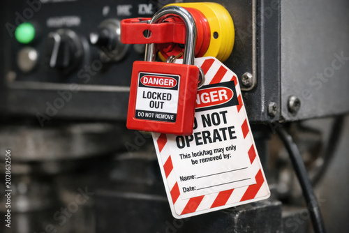 Close up of lockout safety system with red padlock and warning label. tag hangs on heavy machinery control, representing serious workplace safety compliance concept