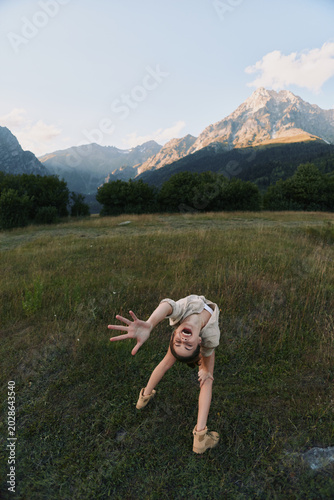 Bild auf Leinwand Young woman in a sunlit meadow reaches toward the camera with a playful pose as a gentle breeze rustles grasses around her, creating a sense of freedom