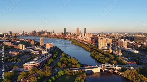 Golden hour aerial drone view of the Boston skyline, featuring the Prudential and John Hancock towers rising above the historic Back Bay neighborhood and the calm waters of the Charles River.