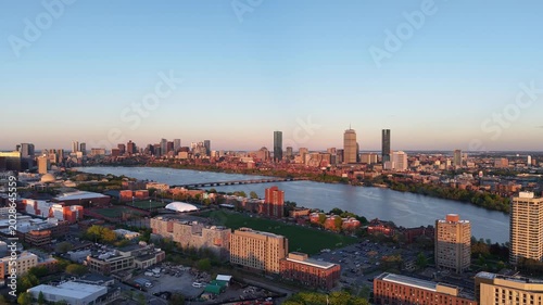Golden hour aerial drone view of the Boston skyline, featuring the Prudential and John Hancock towers rising above the historic Back Bay neighborhood and the calm waters of the Charles River.