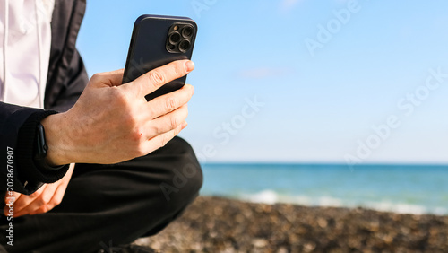 Tableau sur toile Person viewing mobile on oceanfront stones