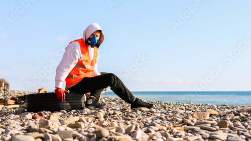 Foto Sitting masked person holding tire on polluted pebble beach