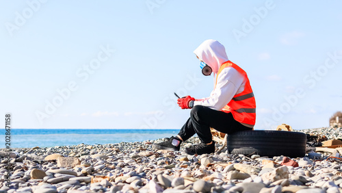 Masked activist takes break on tire at beach cleanup site