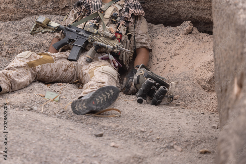 Fototapeta premium Soldier rests on ground with weapon and gear in conflict area