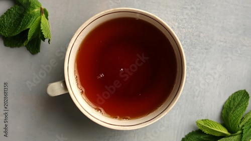 Photography A cup of black tea surrounded by fresh mint leaves on a light background, top view
