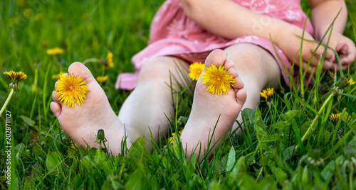 Slika na platnu Close-up of child barefoot feet with yellow dandelion flower on green grass in summer