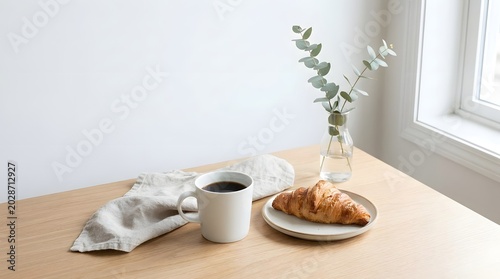 Bright and minimalist breakfast setting with a warm croissant, black coffee, and eucalyptus decor.