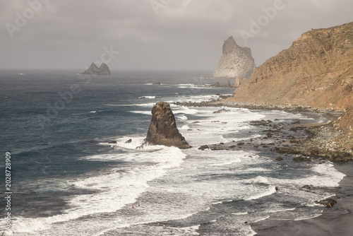Quadro su tela Rugged Coastline Benijo, Tenerife: Jagged sea stacks rise dramatically from the churning ocean waves along a rocky, windswept coastline under a dramatic, cloudy sky