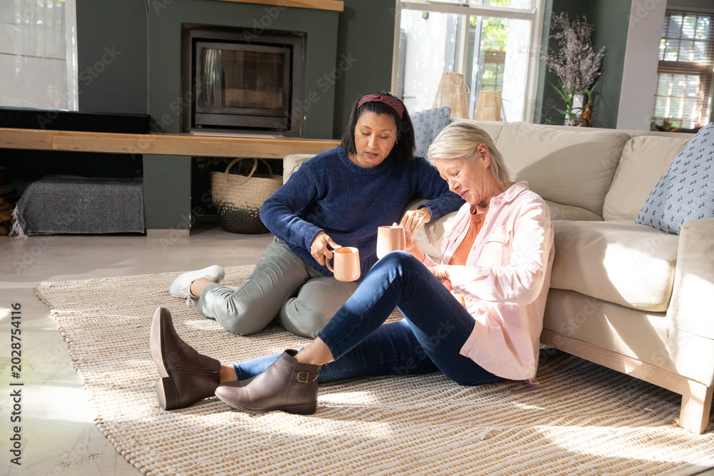 Fototapeta premium Two women sitting on rug with mugs pointing at paper causing animated decor swatches changing sofa