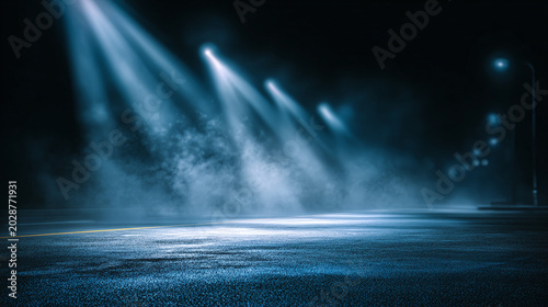 Spotlights illuminate a foggy, deserted street at night, casting dramatic blue beams through the mist, creating an atmospheric and mysterious scene.