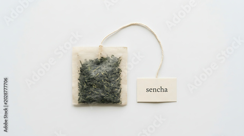 A single sencha green tea bag with paper tag and string isolated on a minimalist white background for healthy beverage concept