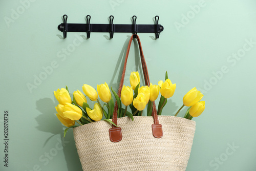 Yellow tulips in wicker bag hanging on green wall, closeup