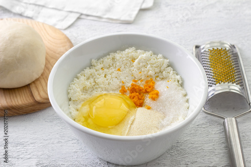 Ingredients for ricotta cheese filling in white bowl with raw egg orange zest semolina and sugar on kitchen table