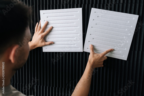 Foto Person positioning white acoustic insulation panels on a black soundproof foam wall, preparing a studio for optimal audio performance and effective sound dampening