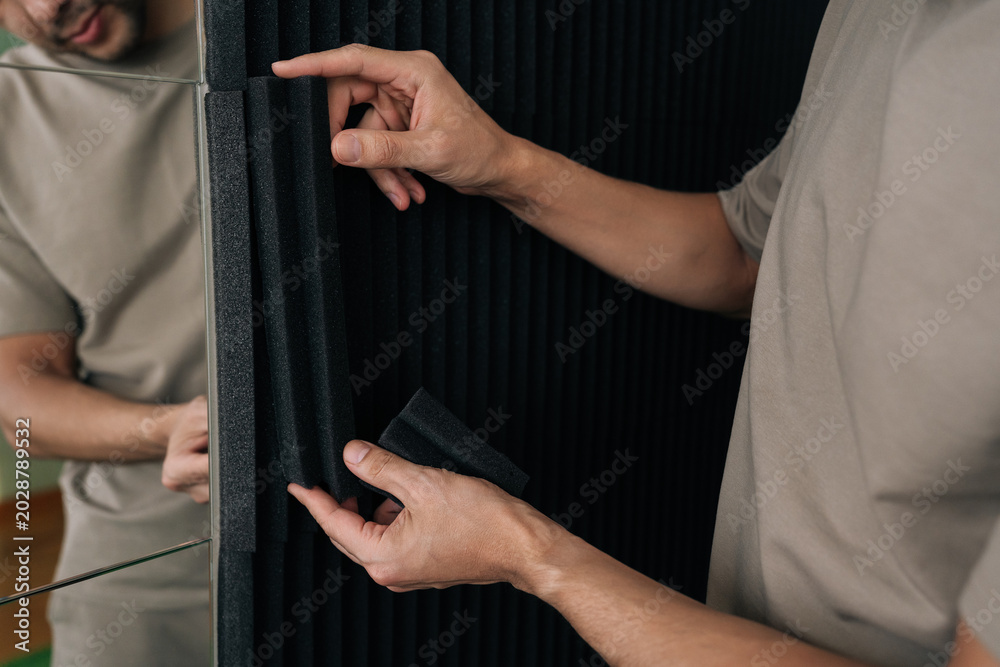 Obraz premium Person installing black acoustic foam soundproof panels on a wall, enhancing sound insulation and improving room acoustics for recording studios or home theaters.