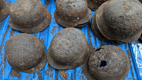 Canvastavla Heavily rusted World War II steel helmets as archaeological ground finds with visible corrosion