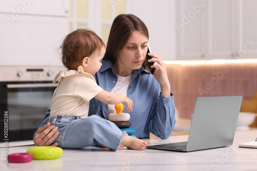 фотографія Young mother working and her baby playing with toy in kitchen at home