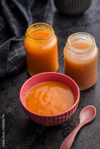 Creamy Pumpkin Soup in Pink Bowl with Glass Jars and Spoon on Dark Surface