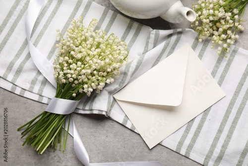 Beautiful lily-of-the-valley flowers, envelope and teapot on grey table, flat...