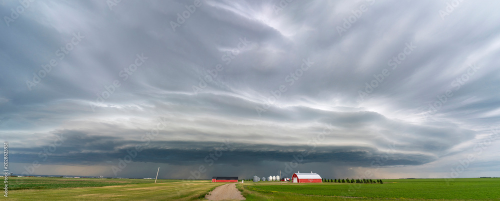 Fototapeta premium Dramatic shelf cloud looms over a rural farm with red barn and silos