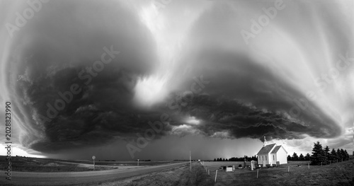 Dramatic storm clouds gather over a small white church and cemetery