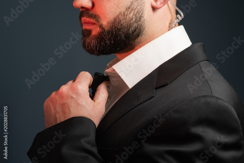 Bearded security guard adjusting a collar microphone or talking into a secret service transmitter button, close-up crop on suit.