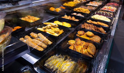 Supermarket ready food counter with fried fish, cutlets, chops, and other freshly cooked dishes on display. Hot meal section close-up.