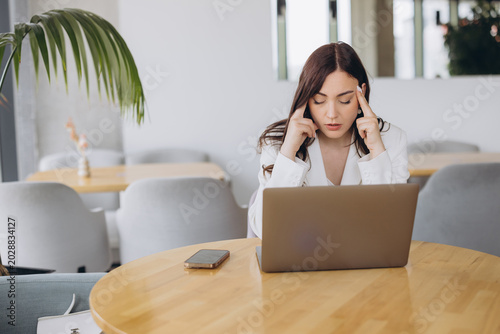 Quadro su tela Young businesswoman with headache due to stress and burnout, working on a laptop