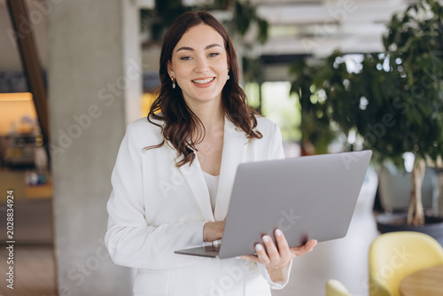 Foto Professional woman standing, smiling and working on laptop, managing business in