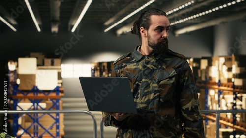 Photos Male army officer checking storage shipment route in a military base, adult man supervising logistics operations and ensuring cargo inspection