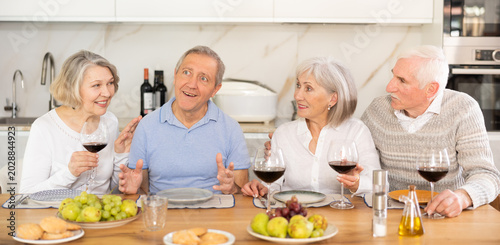 Fotografía At the table, happy group of adults enjoy their holiday, drink red wine and talk