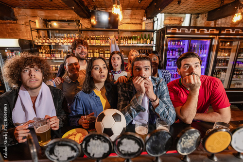 Foto Anxious sports fans staring ahead in nervous suspense at a pub bar counter