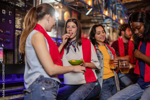 Canvastavla Female friends eating chips and drinking beer while waiting for a soccer match