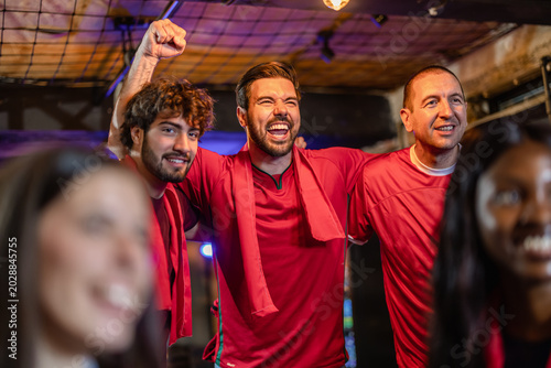 фотографія Three male sports fans in red jerseys cheering intensely for their football team
