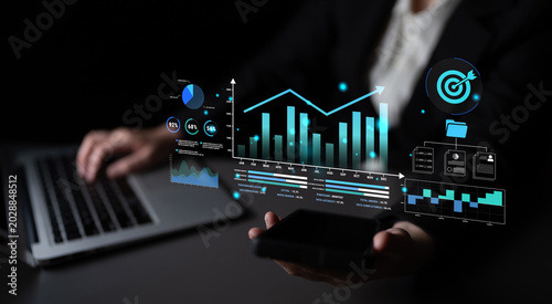 Tableau sur toile Business Professional Analyzing Data with Graphs and Charts on a Laptop and Smartphone in a Dark Office Environment Haptic