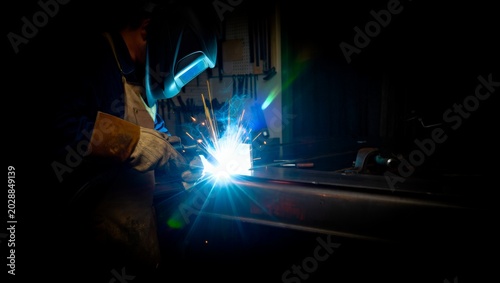 Foto Welder in protective helmet and leather gloves welding dark steel in a dimly lit workshop