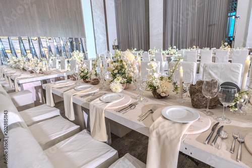 Elegant wedding reception table setting with white floral centerpieces, candles and stone chargers. Luxury banquet dinner decor at wedding venue.