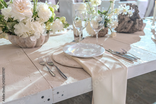 Elegant wedding reception table setting with white floral centerpieces, candles and stone chargers. Luxury banquet dinner decor at wedding venue.