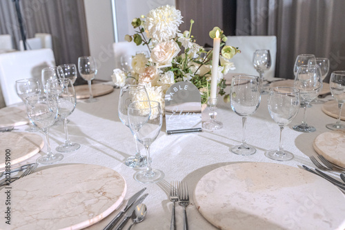 Elegant wedding reception table setting with white floral centerpieces, candles and stone chargers. Luxury banquet dinner decor at wedding venue.