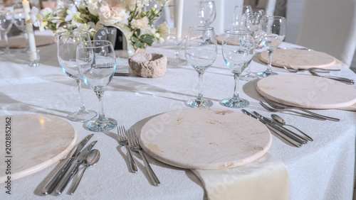 Elegant wedding reception table setting with white floral centerpieces, candles and stone chargers. Luxury banquet dinner decor at wedding venue.