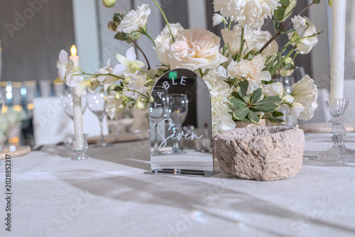 Elegant wedding reception table setting with white floral centerpieces, candles and stone chargers. Luxury banquet dinner decor at wedding venue.