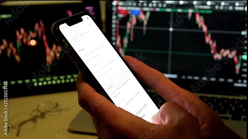 Man hands holding smartphone with AI chatbot showing trading analysis text in front of stock market monitors with charts. Concept of fintech, AI trading assistant, investment and market analysis.