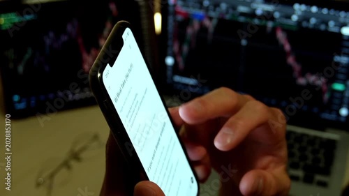 Man hands holding smartphone with AI chatbot showing trading analysis text in front of stock market monitors with charts. Concept of fintech, AI trading assistant, investment and market analysis.