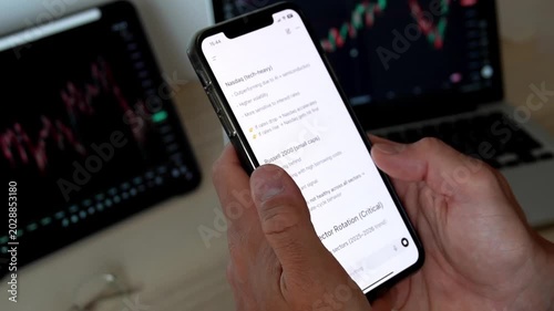 Man hands holding smartphone with AI chatbot showing trading analysis text in front of stock market monitors with charts. Concept of fintech, AI trading assistant, investment and market analysis.